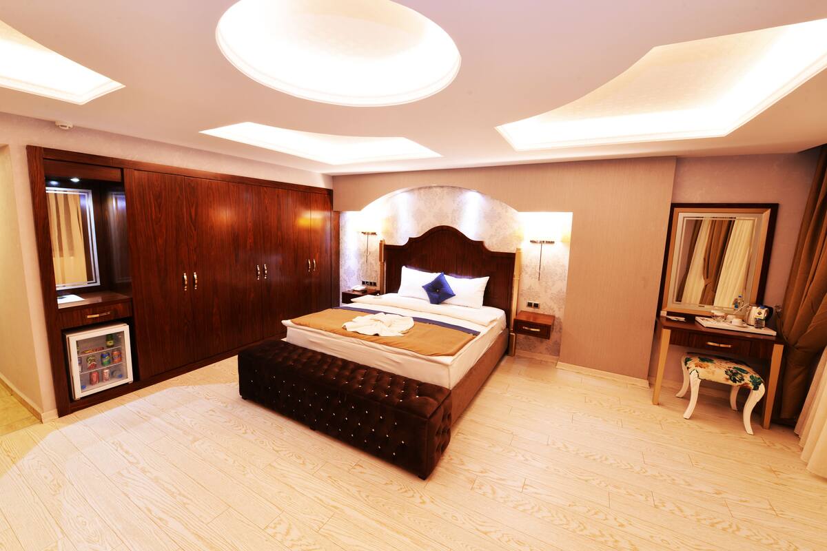 Une chambre à coucher moderne avec un grand lit, une armoire en bois, une petite commode et une coiffeuse avec un miroir.