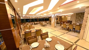 Un restaurante amplio con varias mesas y sillas, que presenta un diseño de techo moderno y ventanas grandes.