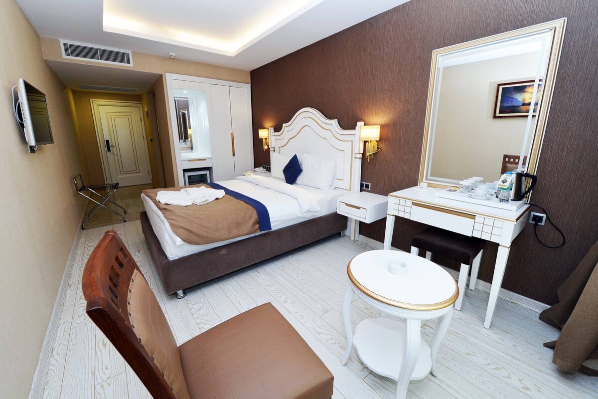 Une chambre d’hôtel avec un lit, une table de chevet, une chaise et un grand miroir.