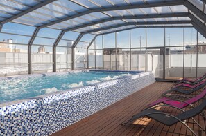 A rooftop swimming pool with a glass enclosure, wooden deck, and lounge chairs. - Funway Academic Resort - Adults Only (Madrid)
