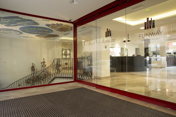 A modern interior with a glass entrance, a staircase with decorative railings, and a sign for Funway Academic Resort. - Funway Academic Resort - Adults Only (Madrid)