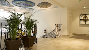 A lobby with a tiled floor, potted plants, a decorative ceiling, and a wall-mounted artwork. - Funway Academic Resort - Adults Only (Madrid)
