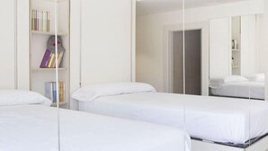 A hotel room with two beds, a bookshelf with books, and a mirror reflecting the room. - Funway Academic Resort - Adults Only (Madrid)