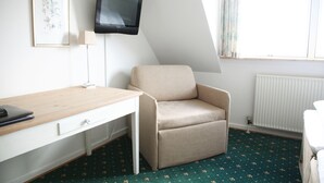 Una habitación con escritorio, silla, televisor, lámpara y ventana con cortinas.