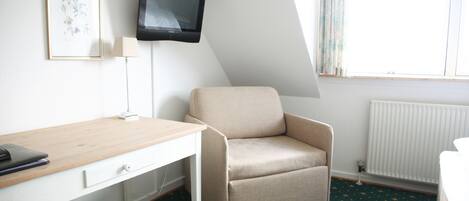 A room with a desk, a chair, a TV, a lamp, and a window with curtains.