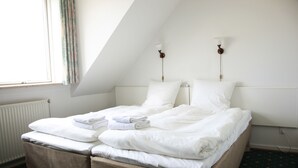 Una cama individual en una habitación con techo inclinado, ropa de cama blanca y un radiador.