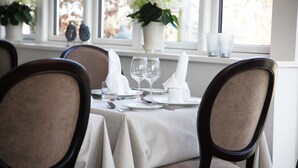 Mesa de comedor lista para cuatro personas, con sillas, un jarrón de flores y vista al exterior.