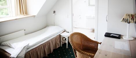 Une petite pièce bien éclairée, avec un lit simple, une chaise, un bureau et une fenêtre avec des rideaux.