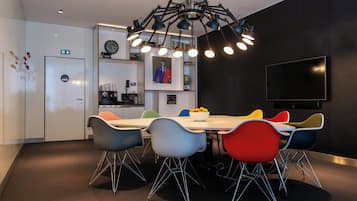Un comedor moderno con una mesa blanca, sillas coloridas y un candelabro negro en el techo.