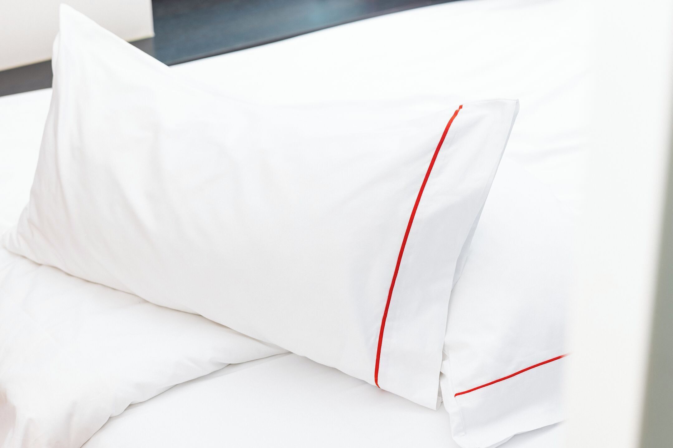 Ein weißes Kopfkissen mit roter Ziernaht auf einem Bett.