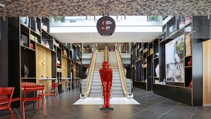 A modern interior with a central escalator, red chairs, and a large red statue.