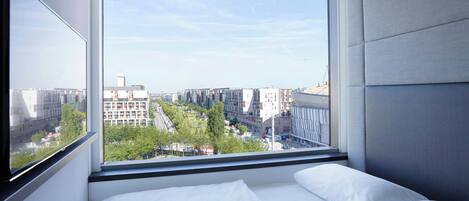 Una habitación de hotel moderna con un gran ventanal que ofrece vistas a la ciudad, una cama con sábanas blancas y un candelabro.