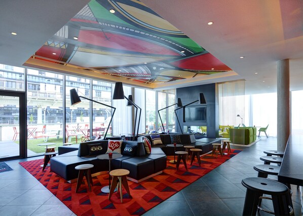 Un espace de détente moderne agrémenté d’une fresque colorée au plafond, de sièges confortables et de grandes fenêtres offrant une vue sur l’extérieur.