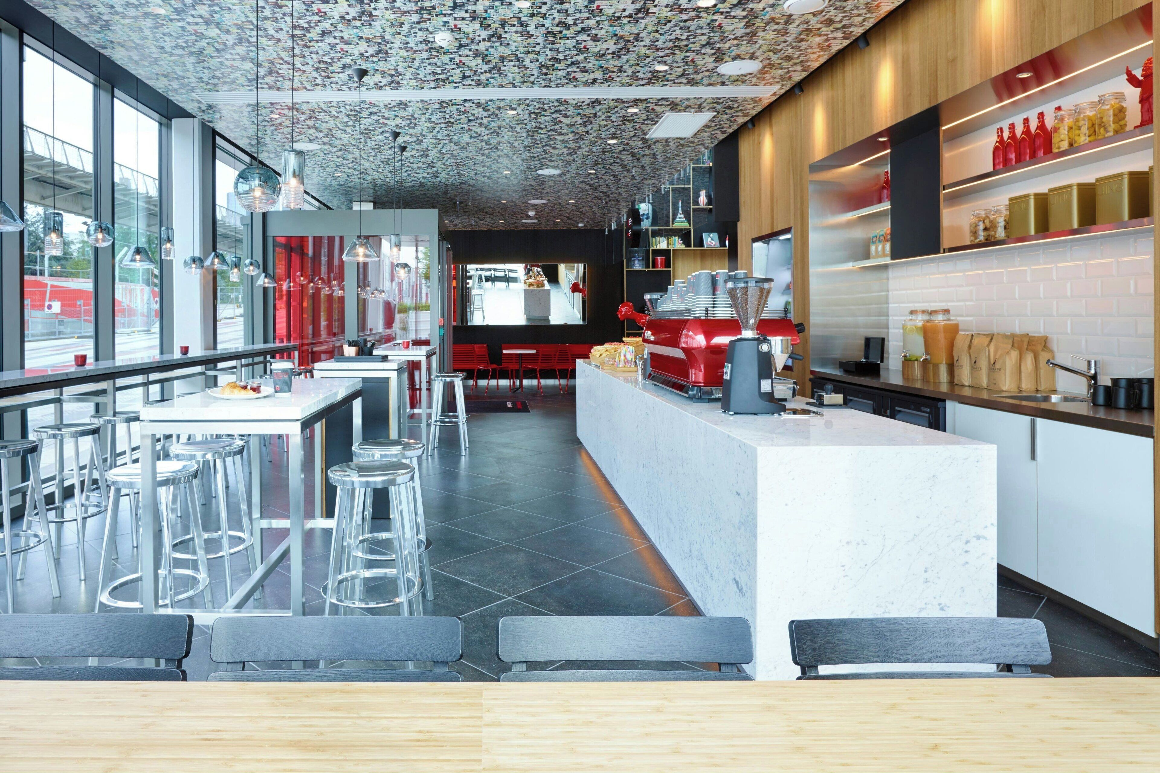 Ein modernes Restaurant mit einer zentralen Bar, hohen Barhocker und Blick auf die Straße durch große Fenster.