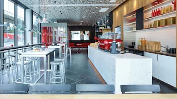 En moderne restaurant med et centralt barområde, høje barstole og udsigt til gaden gennem store vinduer.