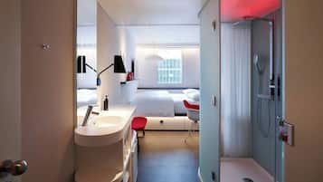 Una habitación de hotel moderna con un ventanal grande, un área de ducha separada y una tocador con lavamanos y espejo.