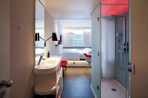Una habitación de hotel moderna con un ventanal grande, un área de ducha separada y una tocador con lavamanos y espejo.