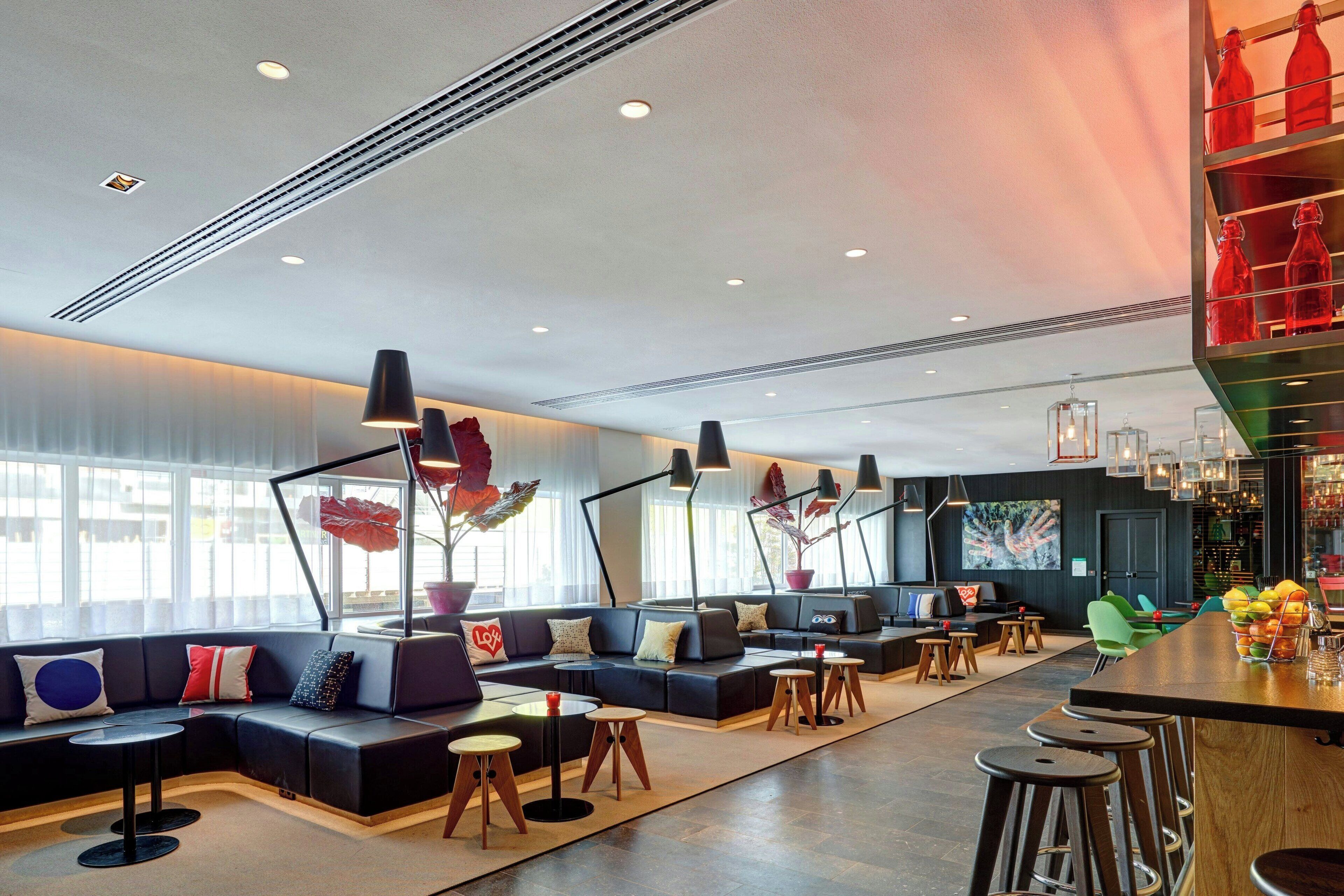 A modern lounge area with a curved seating arrangement, multiple tables, and a bar area with stools.