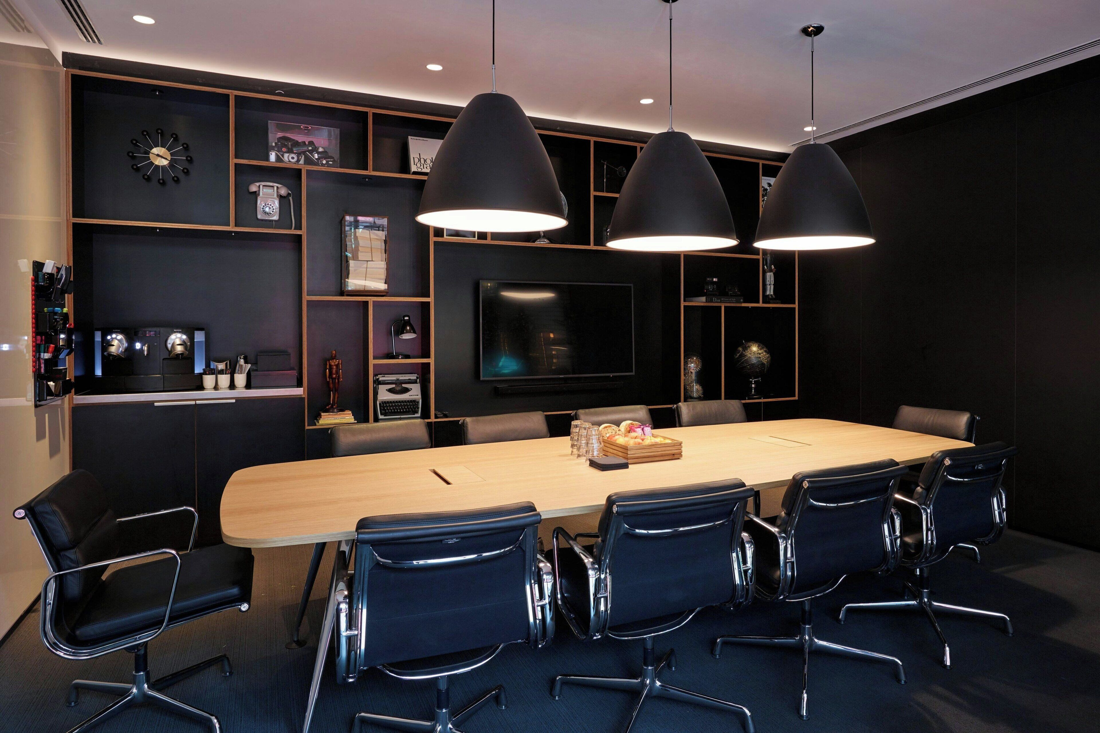 Uma sala de conferência com uma mesa comprida, cadeiras pretas e iluminação pendente.