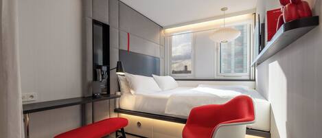 A modern bedroom with a bed, a desk, a chair, and a window with a city view.