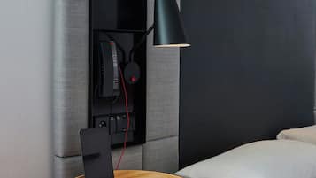 A modern hotel room with a bed, a bedside table with a lamp, and a built-in TV.