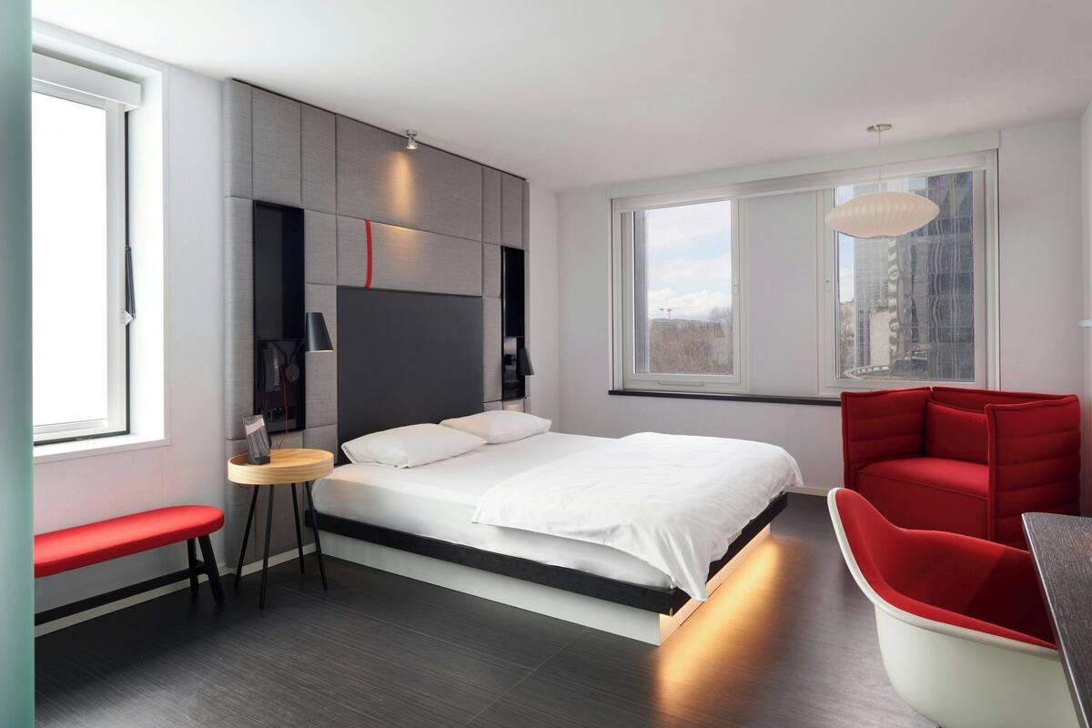 Quarto moderno com uma cama grande, uma mesa redonda pequena, um banco vermelho e uma cadeira vermelha.
