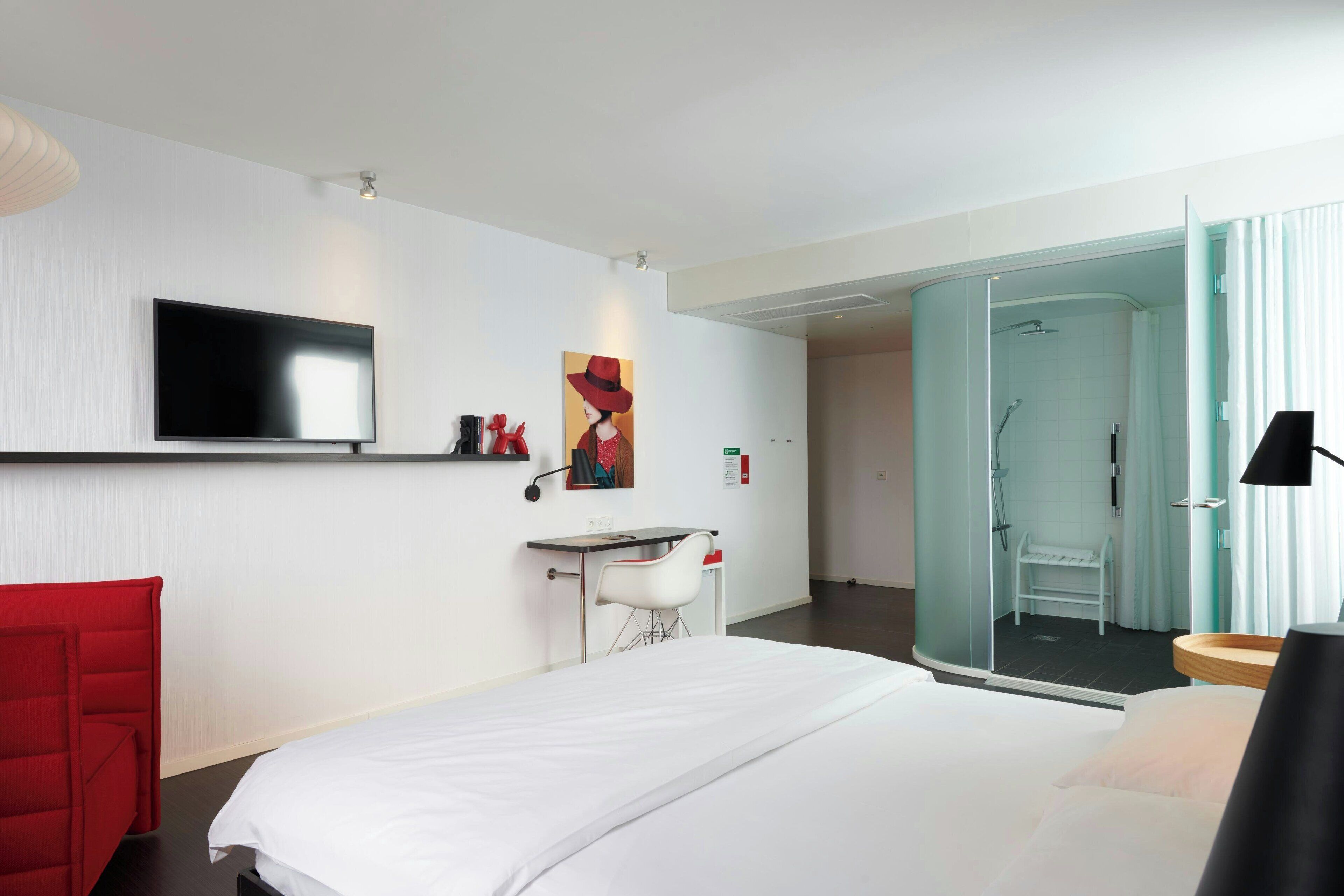 Ein modernes Hotelzimmer mit einem großen Bett, einem Schreibtisch, einem Stuhl, einem Fernseher und einer Duschkabine.