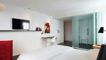 Ein modernes Hotelzimmer mit einem großen Bett, einem Schreibtisch, einem Stuhl, einem Fernseher und einer Duschkabine.