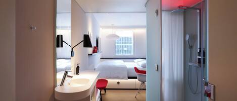 A modern hotel room with a large bed, a separate bathroom with a shower, a sink, and a mirror.