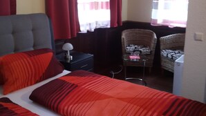 A hotel room with a bed, two chairs, a desk, and a window with curtains.