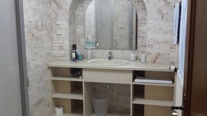 A bathroom with a marble wall, a sink with a mirror, and a toilet.