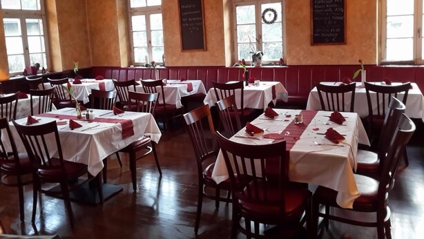A restaurant with multiple tables and chairs, large windows, and a wooden ceiling.
