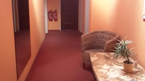 A hallway with a red carpet, a wicker chair, and a table with a potted plant.