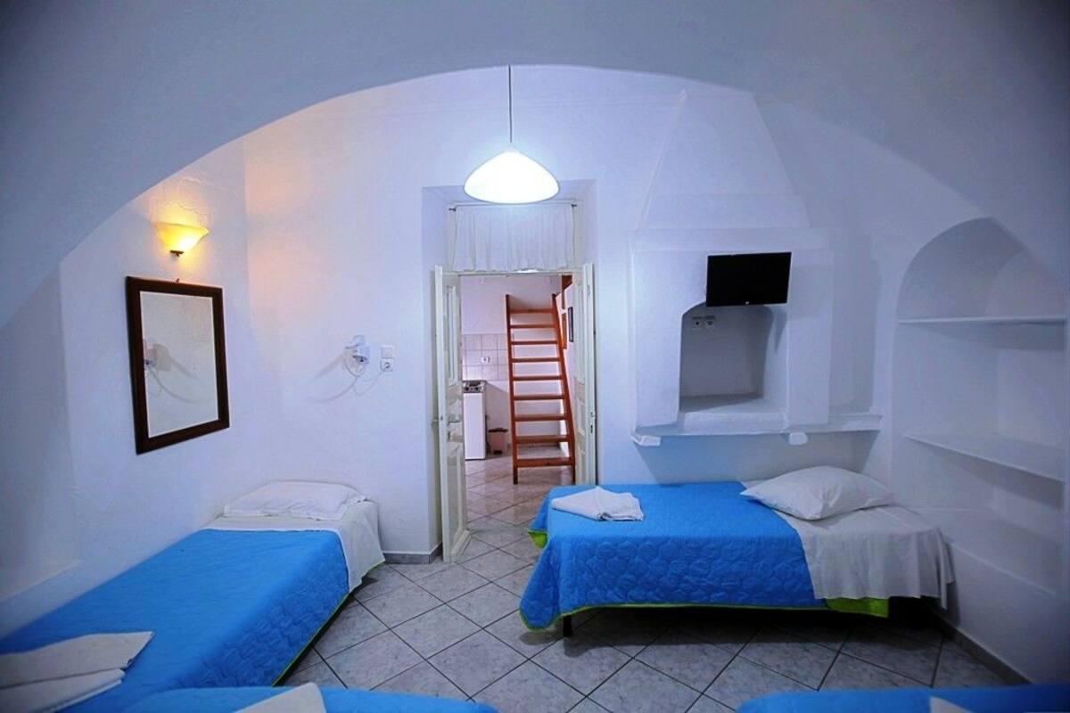 Una habitación pequeña con paredes blancas, dos camas, una escalera y un televisor.
