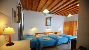 Ein Hotelzimmer mit vier Einzelbetten, Holzbalkendecke, Wandleuchten und einem Fenster mit Vorhängen.
