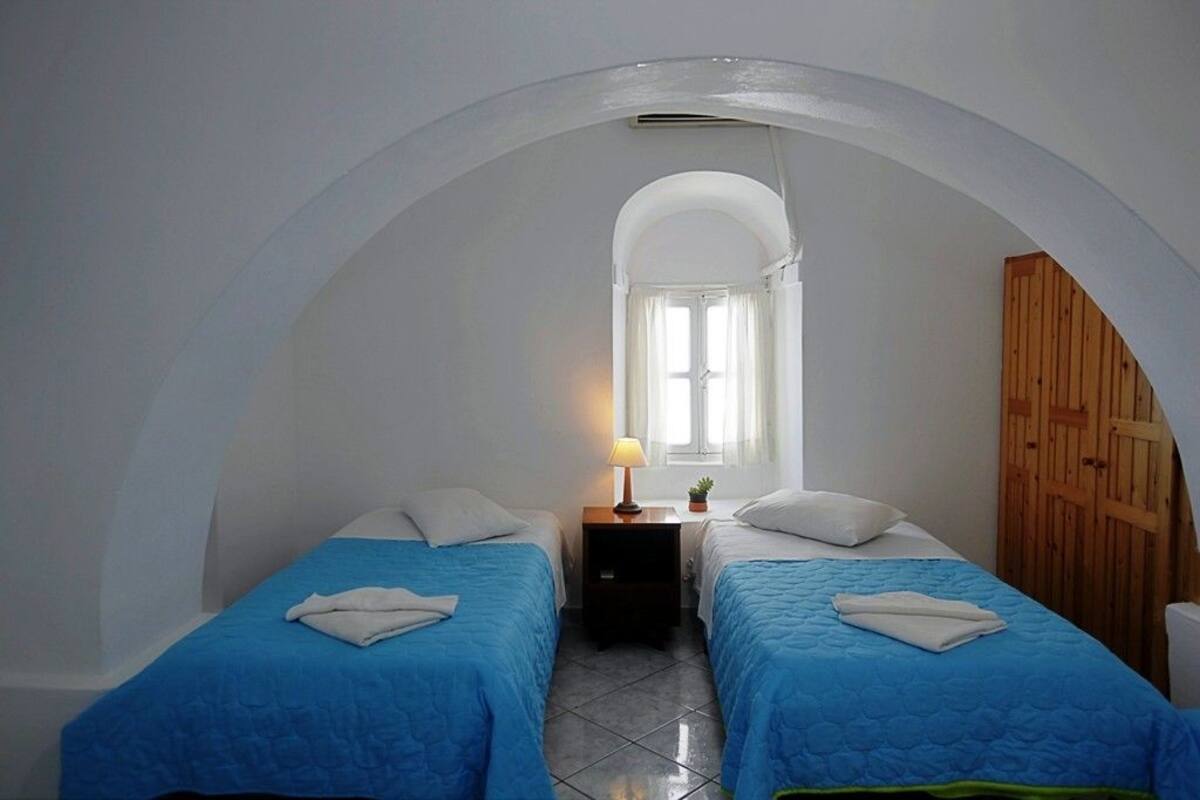 Una habitación con dos camas, una mesita con una lámpara y un armario de madera.