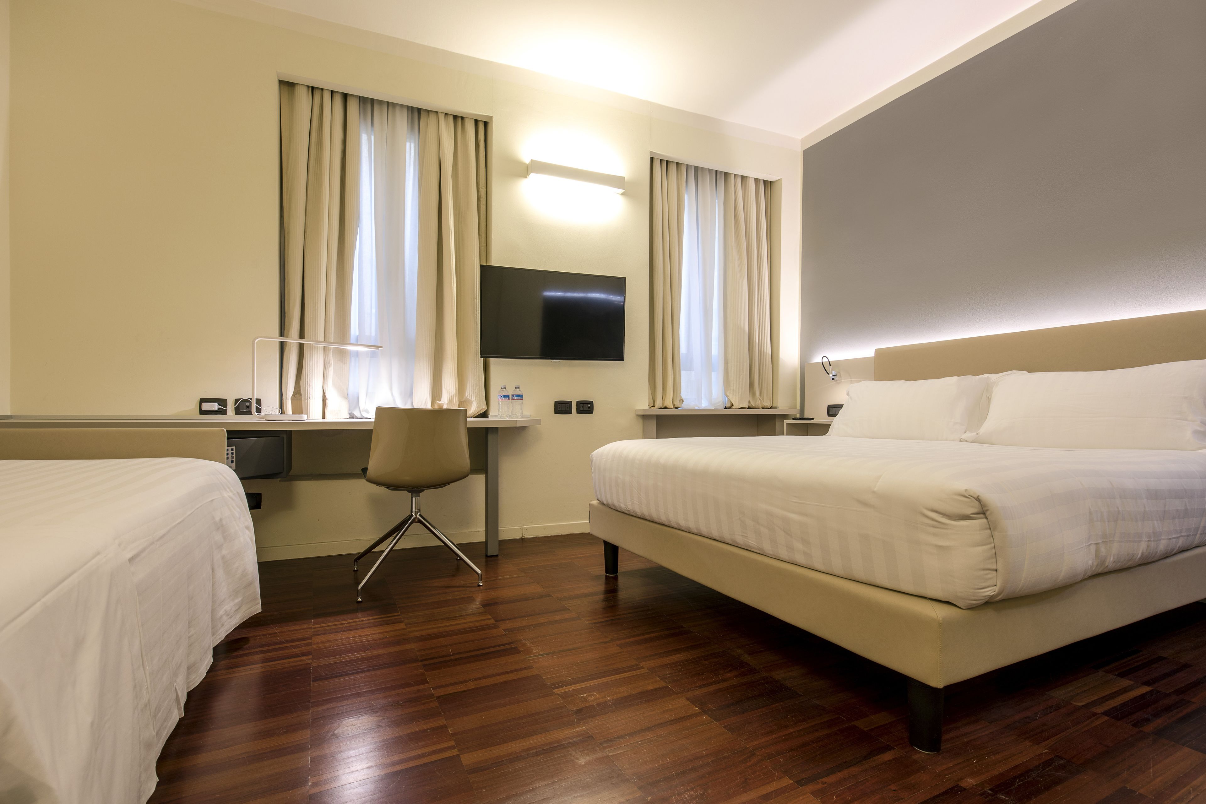 Habitación de hotel con dos camas, un escritorio, una silla, un televisor de pantalla plana y un amplio ventanal con cortinas.