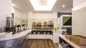 A modern kitchen with a central island, equipped with various appliances and a glass display case filled with fruits and snacks.