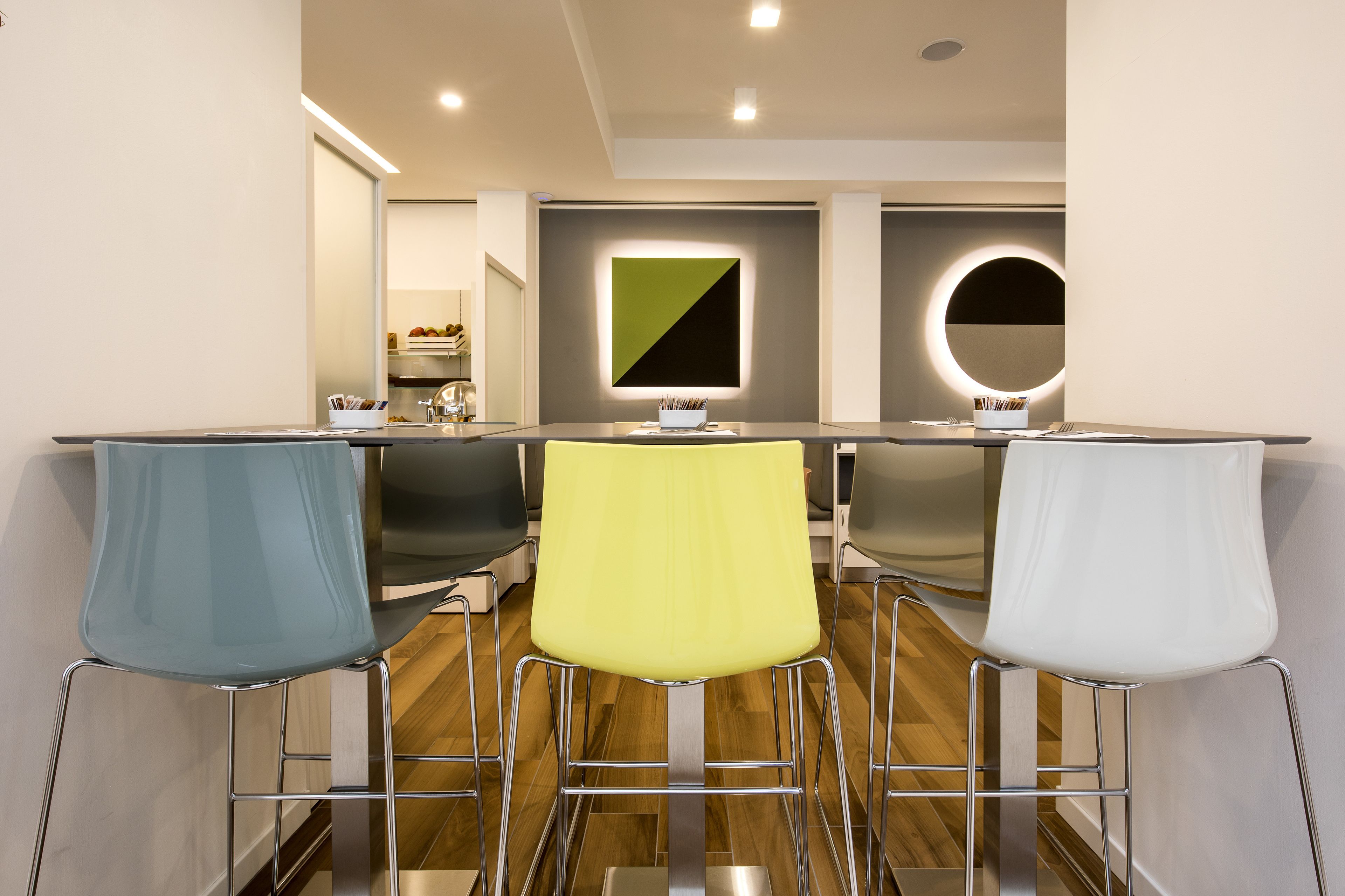 Un espace repas moderne avec une longue table, quatre chaises et un luminaire contemporain fixé au mur.
