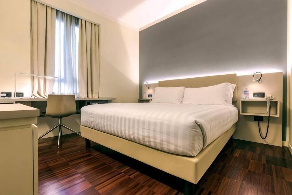 A hotel room with a bed, desk, chair, and a window with curtains.