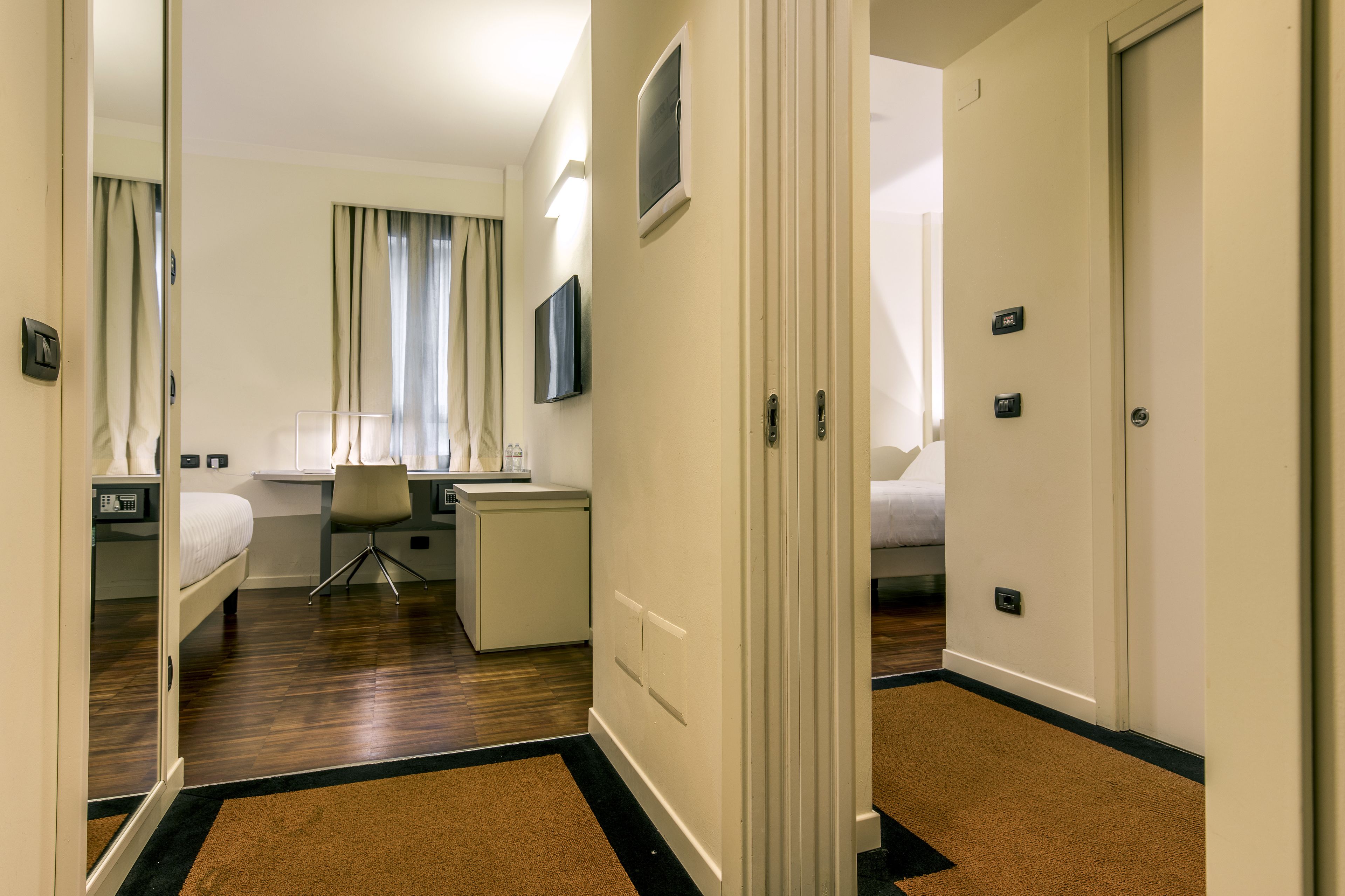A hotel room with a bed, desk, chair, and a small kitchenette.