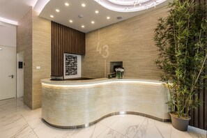 A modern reception desk with a curved design, a wooden panel wall, and a large potted plant to the right.