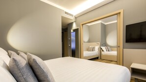 Ett modernt hotellrum med en stor säng, ett sängbord, en spegel och en tv på väggen.