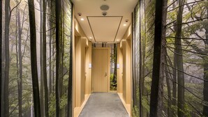 En hall med en väggmålning som föreställer en skog, en trädörr längst ner i hallen och infälld belysning.