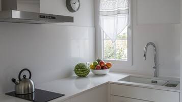 A modern kitchen with a kettle, a bowl of fruit, and a window with a view.