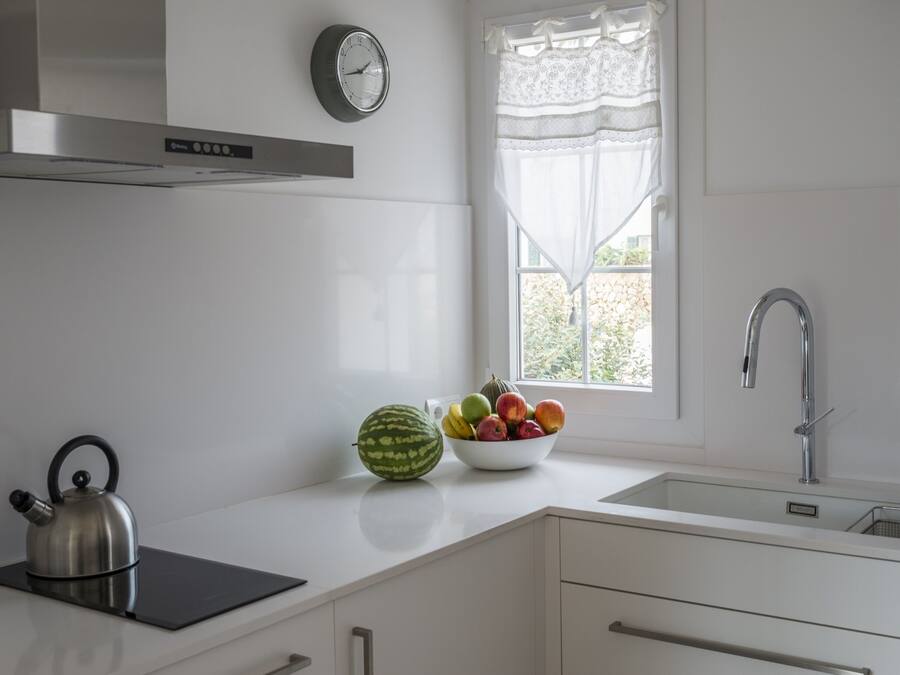 A modern kitchen with a kettle, a bowl of fruit, and a window with a view.