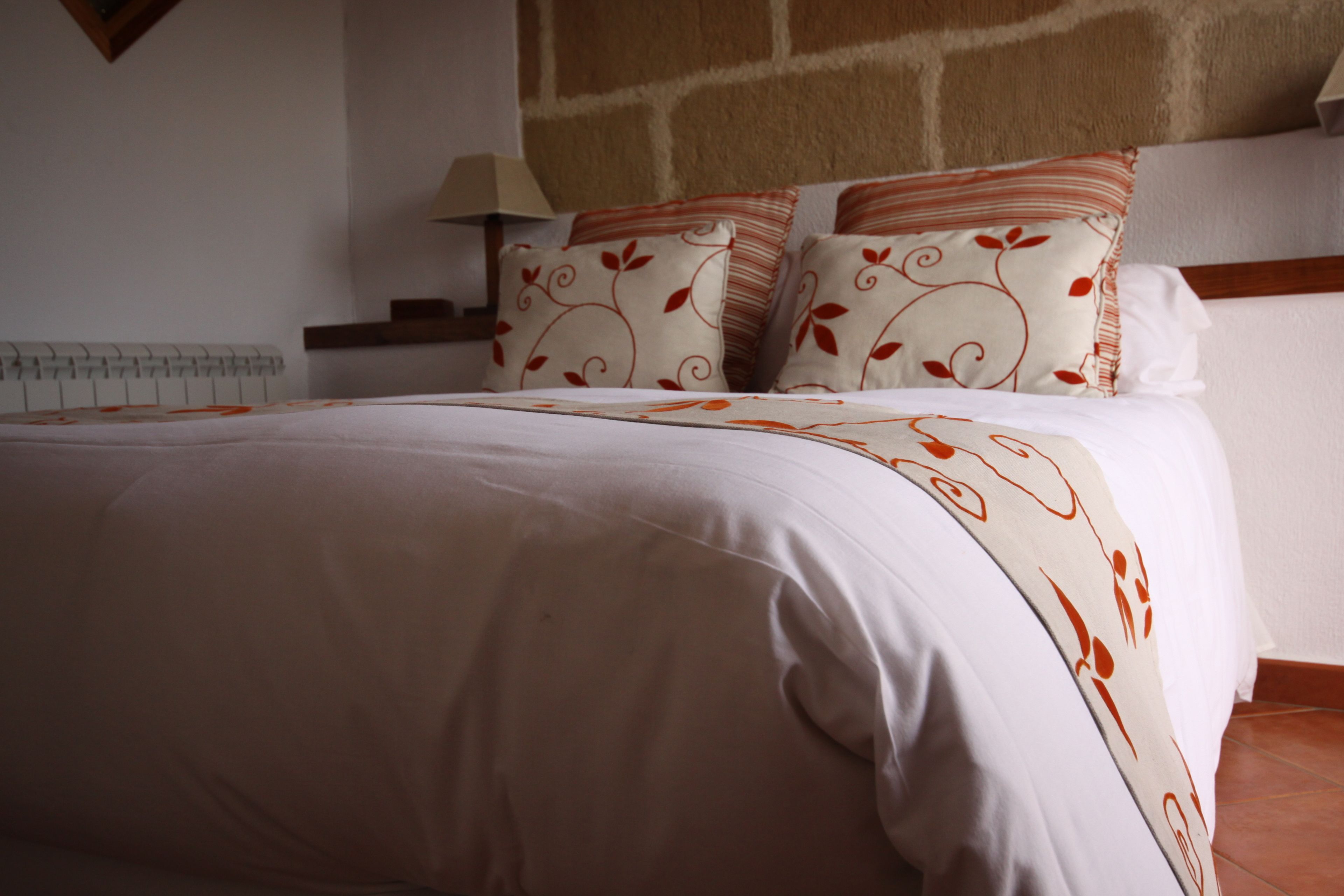 Una cama bien hecha con un edredón estampado, un cabecero de madera y una mesita de noche con una lámpara.