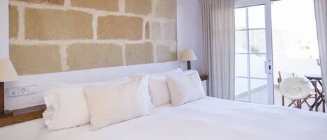 A hotel room with a large bed, a stone wall, a balcony with a chair, and an air conditioning unit.