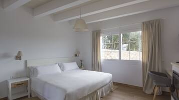 Un dormitorio con una cama grande, una mesita de noche, una lámpara, una silla y una ventana con cortinas.