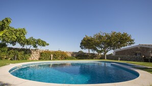 Una piscina circular con un muro de piedra y árboles al fondo.